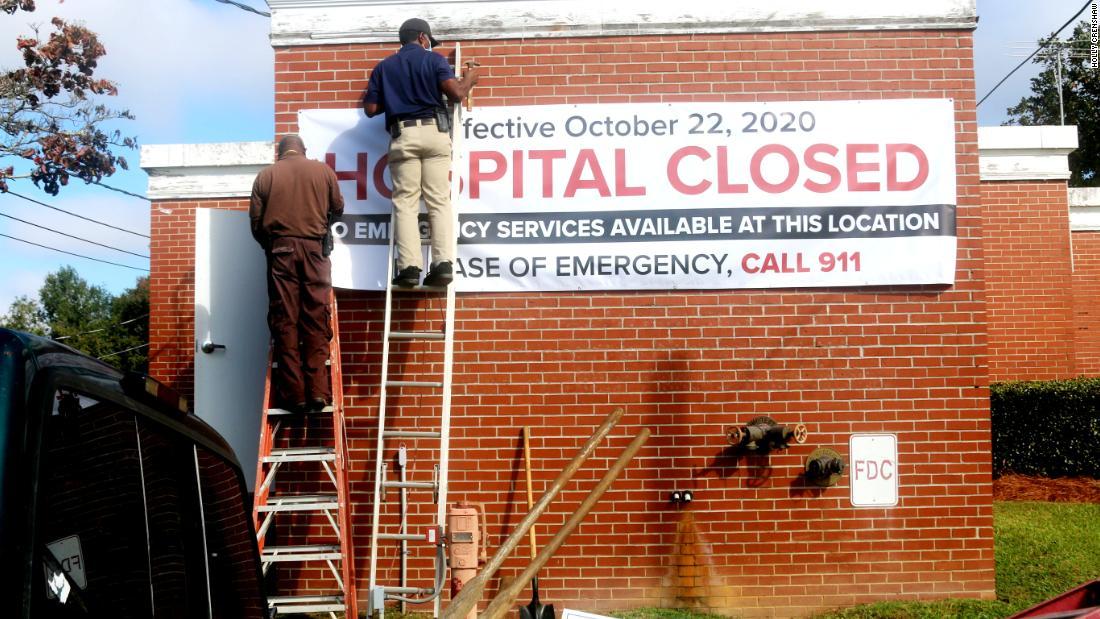 Men climb on ladders and hang a sign announcing a hospital is closed